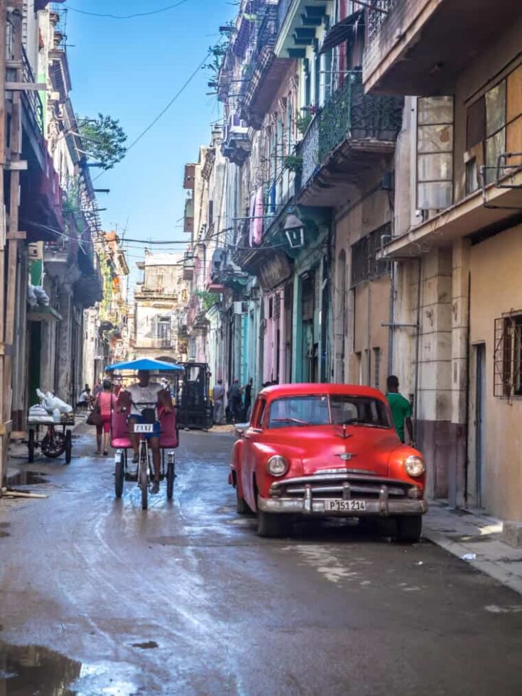 A back street with a red car and man riding a back in Havana, Cuba