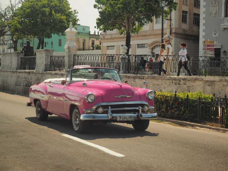 A pink car driving through the streets of Cuba
