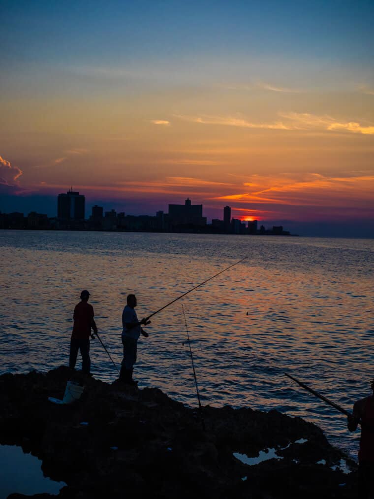 Two people fishing from the rocks at sunset